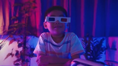 Üç boyutlu film gözlüğü takan, gülümseyen Asyalı çocuk, 3D film gözlükleri takıyor. Mor ve mavi arka planda heyecanlı, eğlence zamanında sanal eski sinema teknolojisi.
