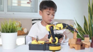 Uzaktan kumandayla tahta bloğu kaldırmak için robot kolu kullanan mutlu Asyalı çocuk, eğlenceli öğrenme başarılı bir ders kontrol robotu kolu, teknoloji bilimi eğitim konsepti.