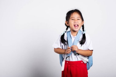 Asyalı sevimli çocuk mutlu bir şekilde gülümsüyor. Tayland üniforması giyiyor. Stüdyoda kırmızı etek, beyaz arka planda izole edilmiş bir şekilde duruyor.