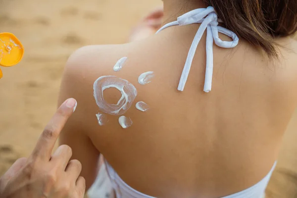 Happy young man applying suntan lotion with sun shape on girlfriend back shoulder at the beach, Asian man on beach applies sunscreen to the skin of woman