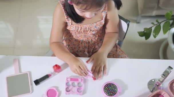 アジアの愛らしい面白い女の子作るメイクディップ筆にボトルにペイント爪ポリッシュ赤爪ニス自分自身 女性であることを学ぶ活動 幸せな子供は化粧品おもちゃで美しい構成されています — ストック動画