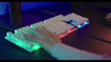 Oyuncuların elleri aktif olarak renkli neon ışıklı tuşlara basıyor, kadın adam oyun klavyesinde ve faresinde yazarak karanlık odada E-spor konseptini kullanarak oyun oynuyor.