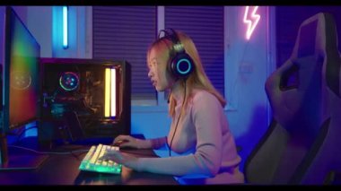 Zafer kazanmak. Asyalı oyuncu çevrimiçi video oyunu oynuyor. Masaüstü bilgisayarında heyecan verici PC renkli neon ışıklar, oyun kulaklığı takan genç kadın bilgisayarını kullanıyor. Başarılı, E-Sport konsepti.