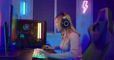 Masaüstü bilgisayarında çevrimiçi video oyunu oynayan Asyalı profesyonel oyuncu renkli neon ışıklı ışıklara, evde oyun oynamak için bilgisayar kullanan oyun kulaklıklı genç bir kadına sahiptir.