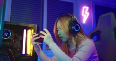 Oyun bitti. Kızgın Asyalı oyuncu oyun kulaklığı takıyor bilgisayar ekranında oyun konsolu oyunu oynuyor evde neon ışığı yanıyor ve maçı kaybettiği için üzgün hissediyor, turnuva oyuncusu E-Sport