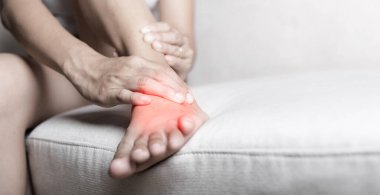 Ayak ağrısı, kanepede oturan Asyalı bir kadın ayak bileği incinmiş, ayaklarında ağrı var, ayak masajı yaptırıyor, el masajı yaptırıyor, ayak bileğinin iç kısmından kas gevşetiyor, sağlık ve sağlık sigortası yaptırıyor.