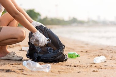Plajı temizlemek için plastik şişeyi çöp poşetine atan gönüllü bir kadın, gün batımında çöpleri temizleyen bir kadın, ekoloji konsepti ve Dünya Çevre Günü, Dünya 'yı Kurtarma Günü.
