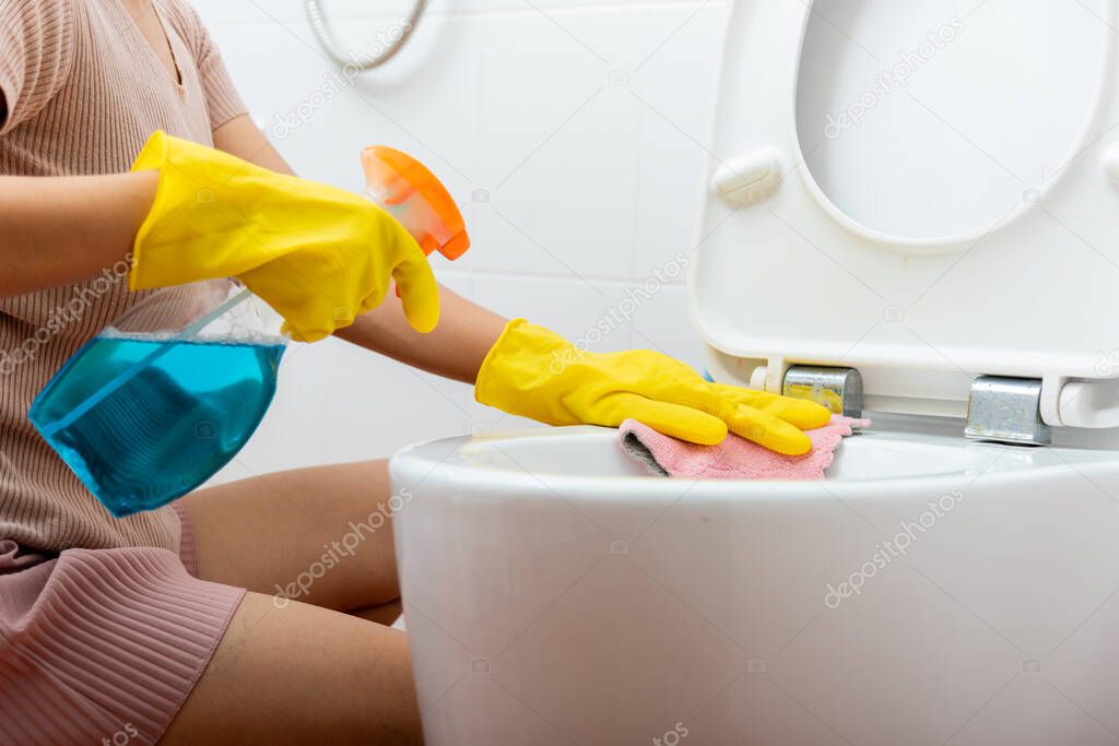 Woman cleaning toilet seat using liquid spray and pink cloth wipe restroom at house, female wearing yellow rubber gloves she sitting and wash cleaner bowl bathroom wc, Housekeeper healthcare concept