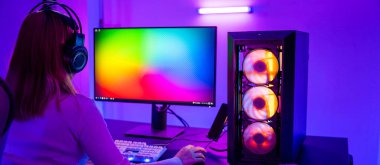 Masaüstü bilgisayarında çevrimiçi video oyunu oynayan Asyalı profesyonel oyuncunun renkli neon ışıklı karanlık odası, oyun kulaklıkları takan genç kadın evde oyun oynamak için bilgisayar kullanıyor, Arka Görüş
