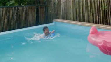 Yüzme havuzunda oynayan mutlu çocuk, şişme yüzükte kıvırcık saçlı mutlu çocuk havuzda eğleniyor ve yaz tatillerinde, tatillerde ve tatillerde sağlıklı açık hava aktivitelerinde tatilde.
