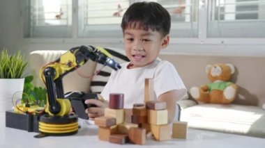 Uzaktan kumandayla tahta bloğu kaldırmak için robot kolu kullanan mutlu Asyalı çocuk, eğlenceli çocuk, başarılı bir ders kontrolü robot kolu, teknoloji bilimi eğitimi alıyor.