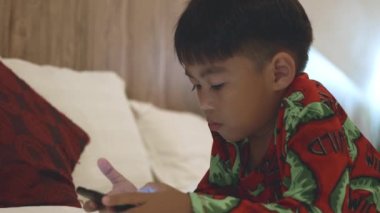 Çocuk evdeki yatak odasında video ve çizgi film izliyor, küçük Asyalı çocuk yatak bağımlılığı oyunu ve çizgi film üzerinde dijital tablet oynuyor, internetteki komik internet kavramı.