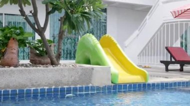 Asyalı küçük çocuk su kaydıraklı bar oyuncağında yüzme havuzu oynuyor mutlu çocuk yaz tatilinde tropikal havuzda oynuyor çocuklar için yüzme sporu öğreniyor.