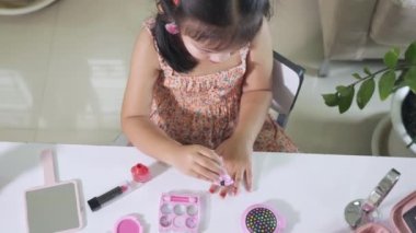 Asyalı sevimli komik küçük kız makyaj malzemelerini şişeye bandırıyor oje sürmek için kırmızı oje sürüyor, kadın olmak için etkinlik öğreniyor, mutlu çocuk güzel makyaj oyuncağıyla makyaj yapıyor.