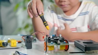 Asyalı çocuk Arduino robot araba ev ödevi projesini evde yapıyor, Küçük çocuk oyuncağı monte etmek için tornavidayla fındığı sıkıyor, elektronik yapay zeka atölyesi dersi oluşturuyor.