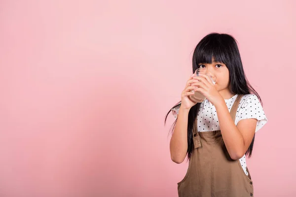 Asian little kid 10 years old smile hold milk glass drink white milk and drinking at studio shot isolated on pink background, Happy child girl daily life health care Medicine food