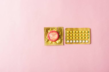 Dünya seks sağlığı ya da AIDS günü, prezervatif paketi ve doğum kontrol hapları hormonal doğum kontrol hapları, pembe arka planda izole edilmiş stüdyo çekimi, güvenli seks ve üreme sağlığı konsepti.