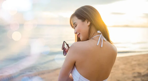 Portrait of young woman in white bikini swimsuit standing posing and holding sunglasses on tropical beach, Happy beautiful Asian girl in swimwear on summer holiday travel