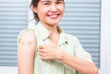 Koronavirüs Covid-19 aşısı aşısı sonrası kolunda yara bandı olan, el hareketi yapan genç bir Asyalı kadın, Coronavirus COVID-19 aşı konsepti.