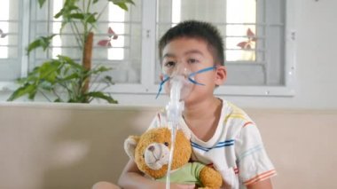 Asian Child using nebulizer mask equipment alone have smoke, Kid boy making makes inhalation nebulizer steam sick cough at home, oxygen spray inhaler therapy, stuffy nose and runny, Health medical