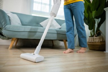 Evde akümülatör süpürgesi olan mutlu Asyalı genç kadın oturma odasında, ev hanımı kadın toz temizleme koltuğun altında ya da elektrikli süpürgeyle mobilya, ev ve ev işi konseptiyle ev hanımı.