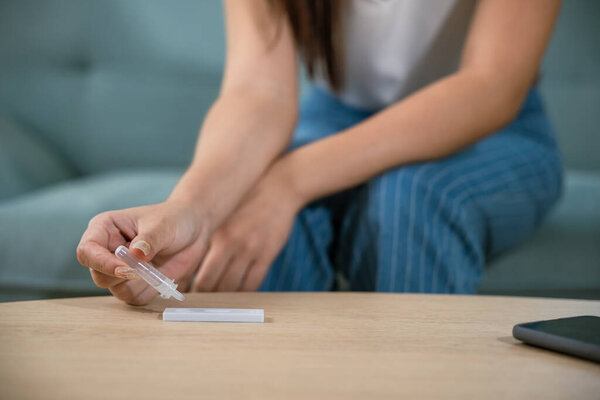 Close up woman hands using rapid antigen test kit for selftest, female four drops of liquid to perform fast coronavirus ATK self test at home in living room on sofa after lockdown and Home Isolation