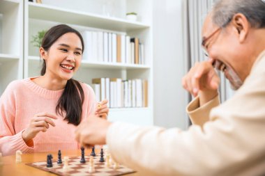 Beautiful young smile woman having fun sitting playing chess game with senior elderly at home, nurse caregiver in nursing home for leisure, Happy active retired people, Healthcare and medical concept