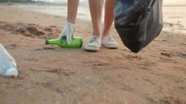 Plajı temizlemek için plastik şişeyi çöp poşetine atan gönüllü bir kadın, gün batımında çöpleri temizleyen bir kadın, ekoloji konsepti ve Dünya Çevre Günü, Dünya 'yı Kurtarma Günü.