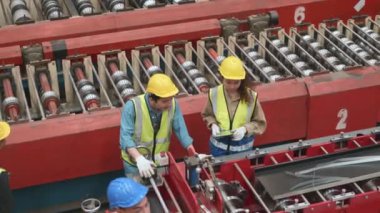 Endüstriyel metal çarşaf fabrikasında makine bakımı yapan bir güvenlik kıyafeti giyen mühendis ve operatör, ekip çalışanı, öğretim görevlisi arkadaşının fabrikada ağır makineyi birçok ekipmanla kontrol etmesine yardım ediyor.