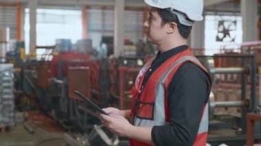 Worker man looking up check list details on a tablet, mechanic is repairing the machine maintenance at metal sheet factory, engineer standing and checking process in industry manufacturing