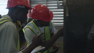 Metal levha fabrikası deposuna sevkiyattan önce iki mühendis Afrikalı siyah işaretli teftiş, fiziksel envanter sayımı, hisse senedi endüstrisini kontrol.