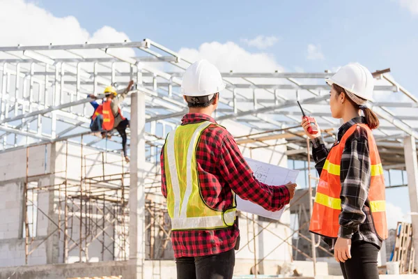 Back two architect and client discussing help create plan with blueprint home building at construction site. Asian engineer foreman worker man and woman meeting talking on drawing paper project