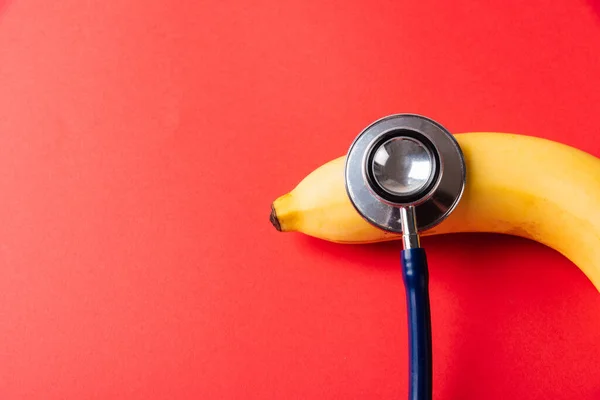 World sexual health or Aids day, Top view flat lay of doctor stethoscope and yellow banana, studio shot isolated on a pink background, Safe sex and reproductive health concept