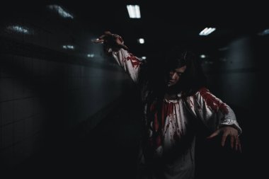 Bloody halloween makeup. Asian woman zombie with blood she death and scary at dark night in tunnel, Horror bloodthirsty ghost girl hair covering face and eye reach arm out, Happy halloween day concept