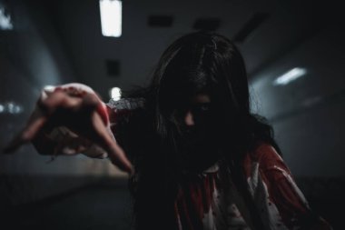 Bloody halloween makeup. Horror bloodthirsty ghost girl hair covering face and eye reach arm out, Asian woman zombie with blood she death and scary at night in tunnel, Happy halloween day concept