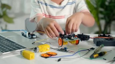 Asian kid boy assembling board into Arduino robot car homework, Little child assemble DC to DC converter into car toy, creating electronic AI technology workshop online school lesson