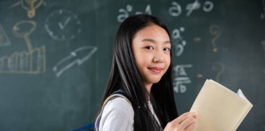 Back to school. Portrait of smiling woman child student of black chalk board, Happy beautiful Asian Schoolgirl girl standing holding books standing in front blackboard of classroom, Education lesson