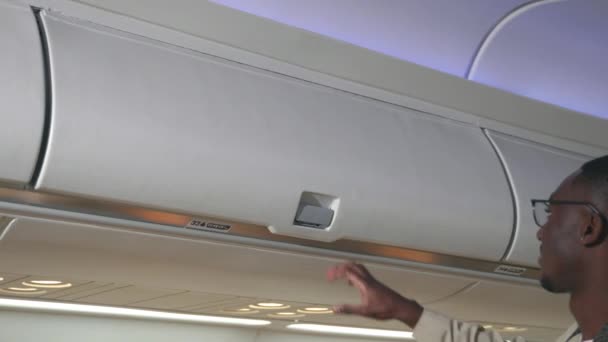 Passagier Schwarzer Mann Legt Gepäck Auf Oberstes Regal Oder Kabinenabteil — Stockvideo