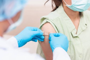 Aşı, Doktor Bey genç bir kadının omzuna koronavirüs aşısı yaptıktan sonra lastik koruyucu eldivenler yapıştırıcı bandaj sıva, Covid-19 İlaç ve Sağlık Konsepti koyuyor.