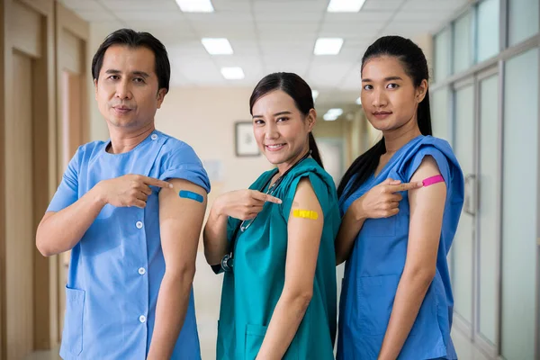Medical personnel pointing to bandage with plaster on arm after getting against Covid-19 vaccine, happy nurse woman and man standing at hospital, Covid-19 vaccination concept