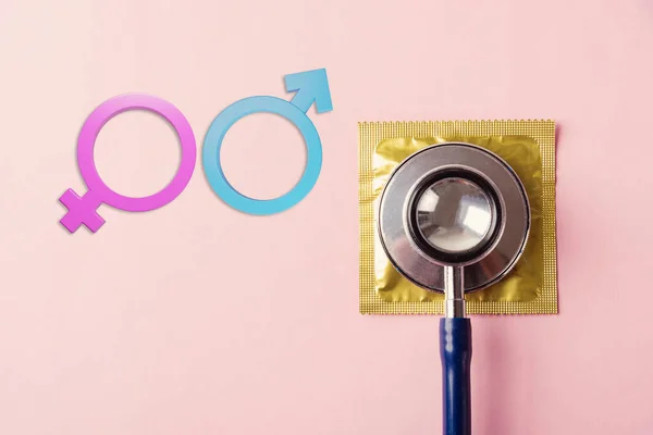 World sexual health or Aids day, Top view flat lay medical equipment, condom in pack, doctor stethoscope and Male and female gender signs, isolated on a pink background, Safe sex reproductive health