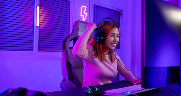 Winning. Young woman in gaming headphones playing video game online at home neon room feel excited, Happy Gamer young plays online video games computer she raises hands to wins tournament, E-Sport