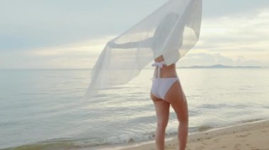 Genç ve güzel bir kadın bikini mayo giyip sarong üfleyerek tropikal plajda yürüyüş yapıyor ve vücut çeviriyor mutlu Asyalı seksi kadınlar dışarıda tatilde eğleniyor, yaz tatili tatilinde dinleniyor.