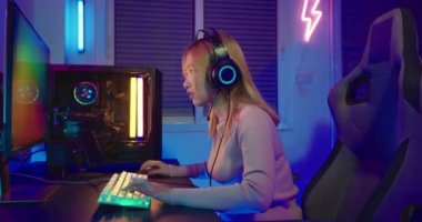 Zafer kazanmak. Asyalı oyuncu çevrimiçi video oyunu oynuyor. Masaüstü bilgisayarında heyecan verici PC renkli neon ışıklar, oyun kulaklığı takan genç kadın bilgisayarını kullanıyor. Başarılı, E-Sport konsepti.