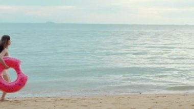 Plajda koşan kauçuk yüzüklü güzel Asyalı kadın, tropik plaj tatili kaçamağında eğlenen bikinili mutlu kadın yaz tatilinde kendini rahat hisseden tatil beldesi.