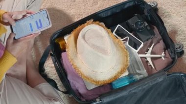 Preparing for travel in new normal. Woman chatting surfing internet use smartphone application during packing suitcase baggage, Female texting message on mobile phone with friend for ready