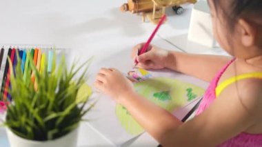 Mutlu çocuk renkli çizim yapan aile kağıt üzerinde el ele tutuşuyor, Asyalı şirin çocuk anaokulu öğrencisi masaya oturuyor evde kalemle resim çiziyor, dünya günü konsepti.