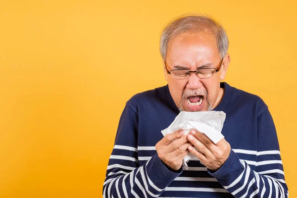 Portrait senior old man blowing nose with tissue studio shot isolated on yellow background, Asian elder man cold having flu and sneezing from sickness virus problem use tissue, pensioner unwell
