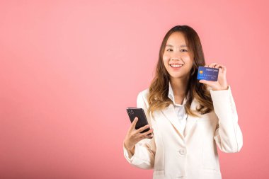 Mutlu bir Asyalı portresi güzel tatlı bir genç kadın gülümseyen cep telefonu ve plastik banka kartı, stüdyo resmi pembe arka planda, akıllı telefon kullanan bir kadın online alışveriş yapıyor.