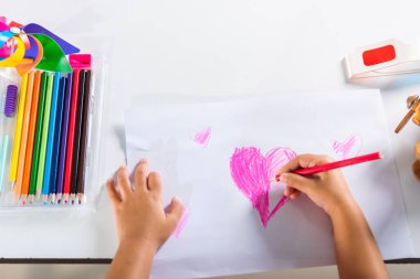 Asyalı şirin çocuk anaokulunda gülümsüyor yaratıcı kalpler çiziyor evde aşk resmi çekiyor mutlu çocuk renkli küçük kız beyaz kağıda pembe kalp çiziyor sevgililer günü ya da anneler günü ya da babalar günü, sanat eğitimi.